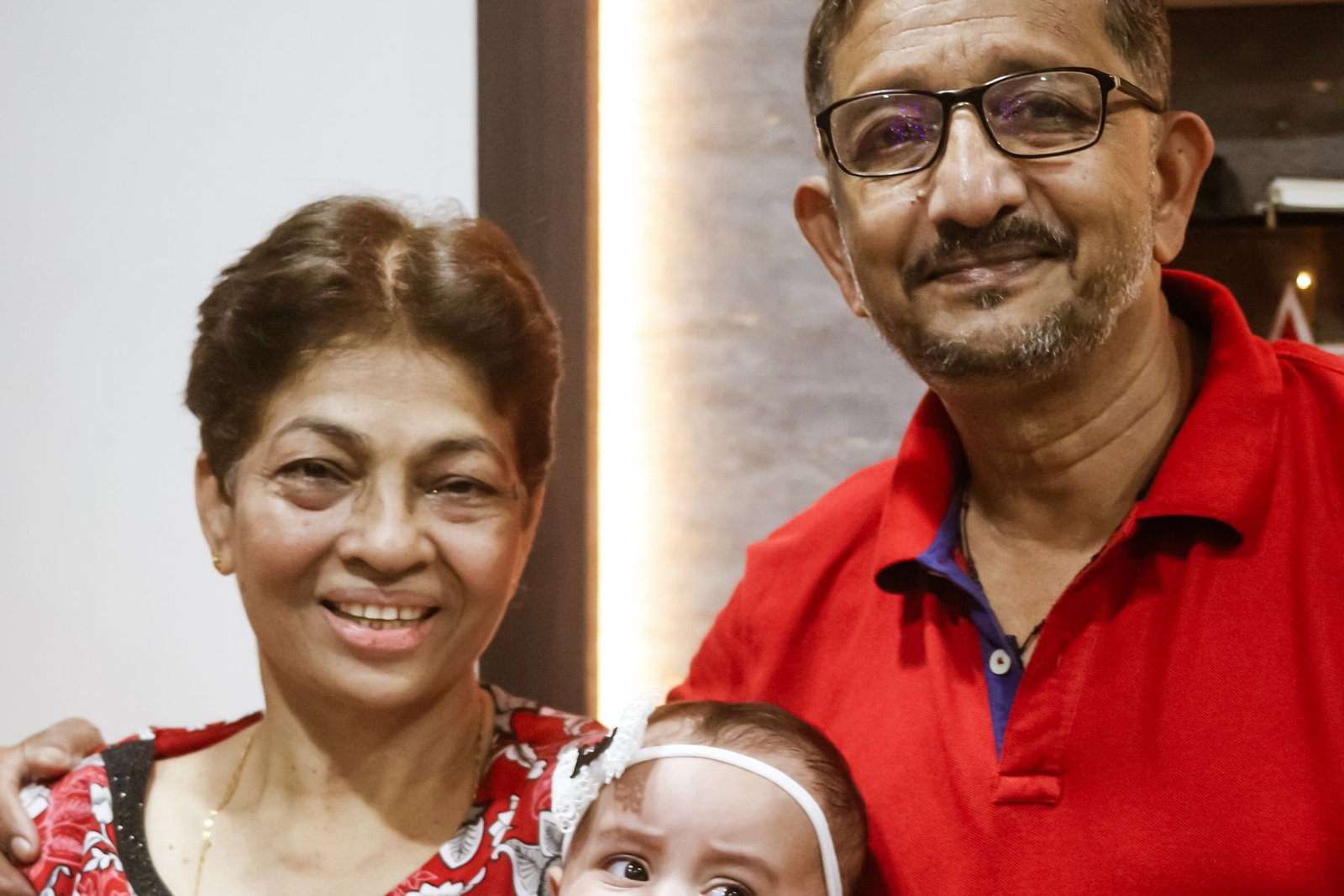 A senior couple smiling at home with their grandchild