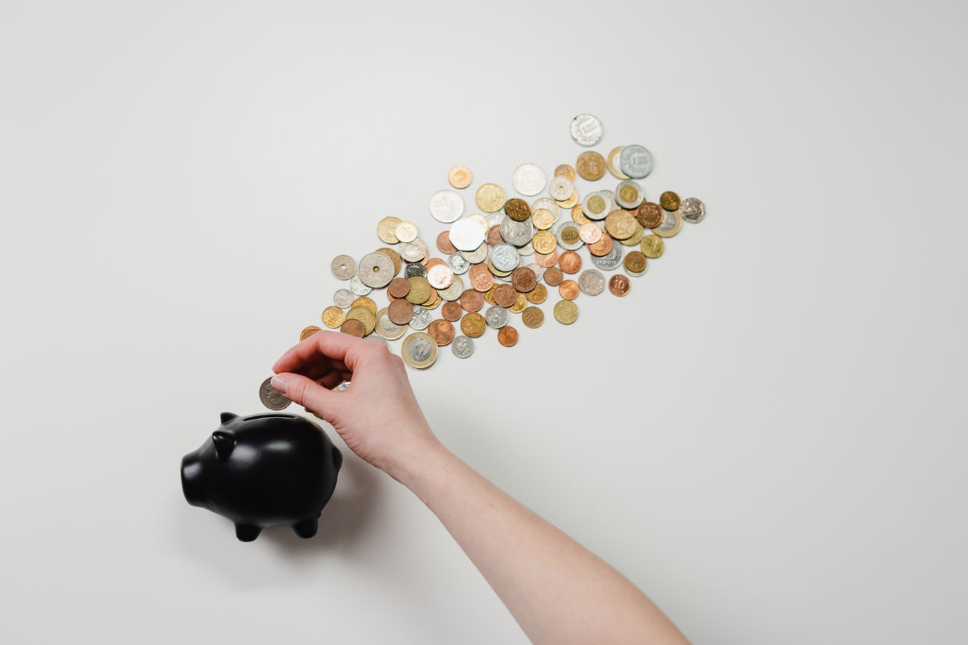 Hand dropping coins into a small black piggy bank